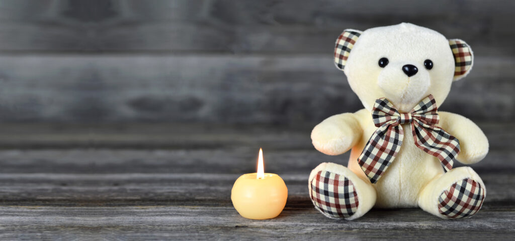 Teddy,bear,and,white,candle,on,wooden,background,with,copy